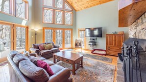 A spacious living room with a high ceiling, large windows, a fireplace, and a television. - Dog Friendly Deep Creek Estate w/ Fire Pit & Dock (MCHENRY)