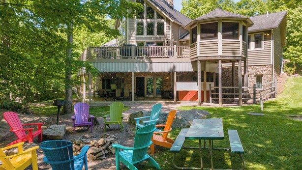 A two-story house with a balcony, outdoor seating area with Adirondack chairs, and a stone fireplace. - Dog Friendly Deep Creek Estate w/ Fire Pit & Dock (MCHENRY)
