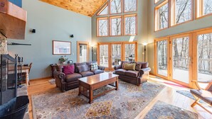 A spacious living room with a fireplace, leather sofas, and large windows offering views of the outdoors. - Dog Friendly Deep Creek Estate w/ Fire Pit & Dock (MCHENRY)