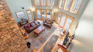 A spacious living room with a stone wall, a fireplace, a large window with a view of trees, and a cozy seating area with a coffee table and sofas. - Dog Friendly Deep Creek Estate w/ Fire Pit & Dock (MCHENRY)