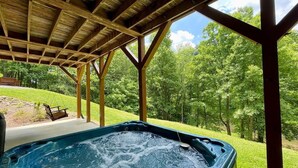 Een hottub onder een houten pergola, met een gazon en bomen op de achtergrond.