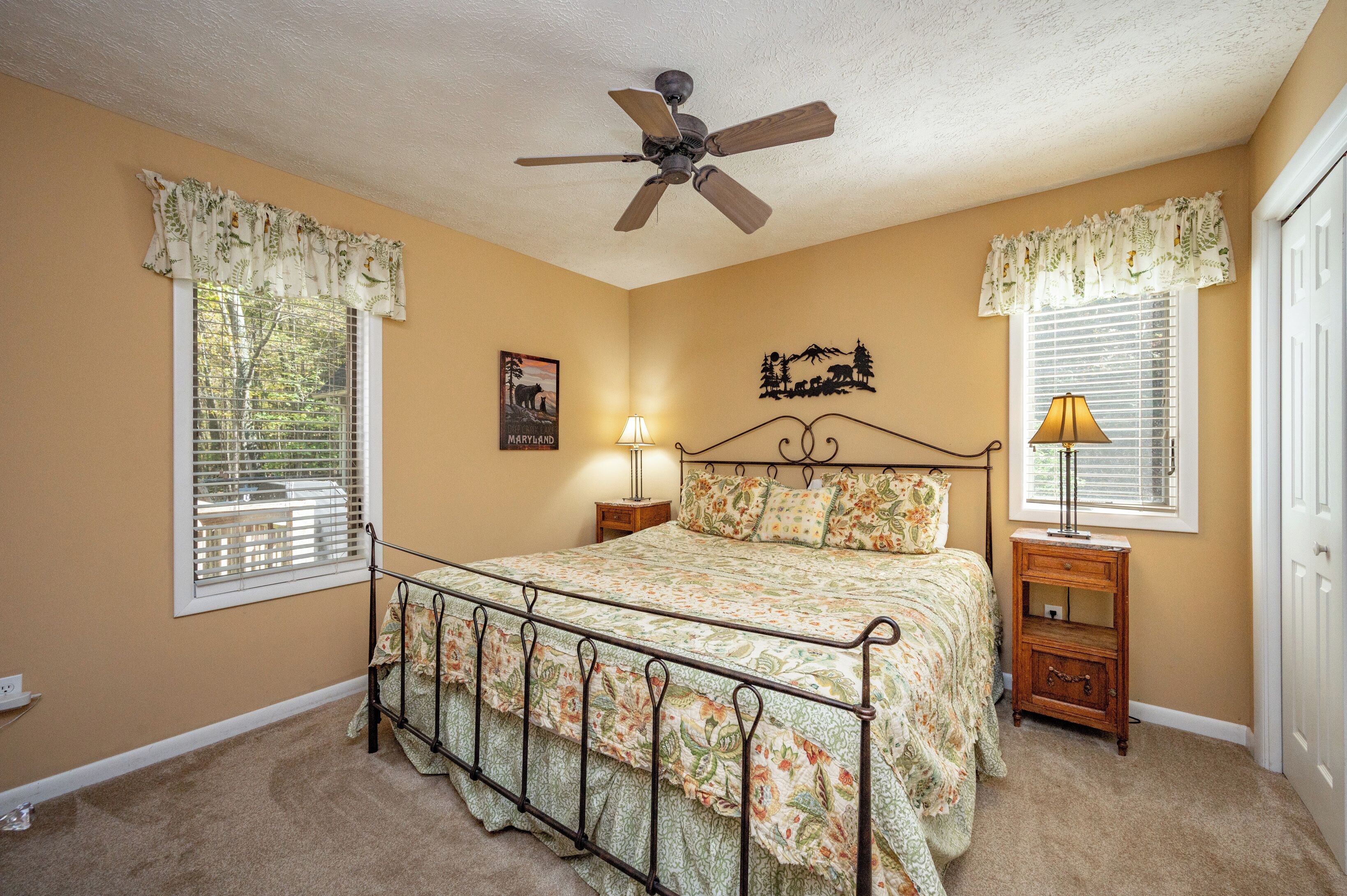 A bedroom with a bed, a ceiling fan, two bedside tables with lamps, and a window with blinds.