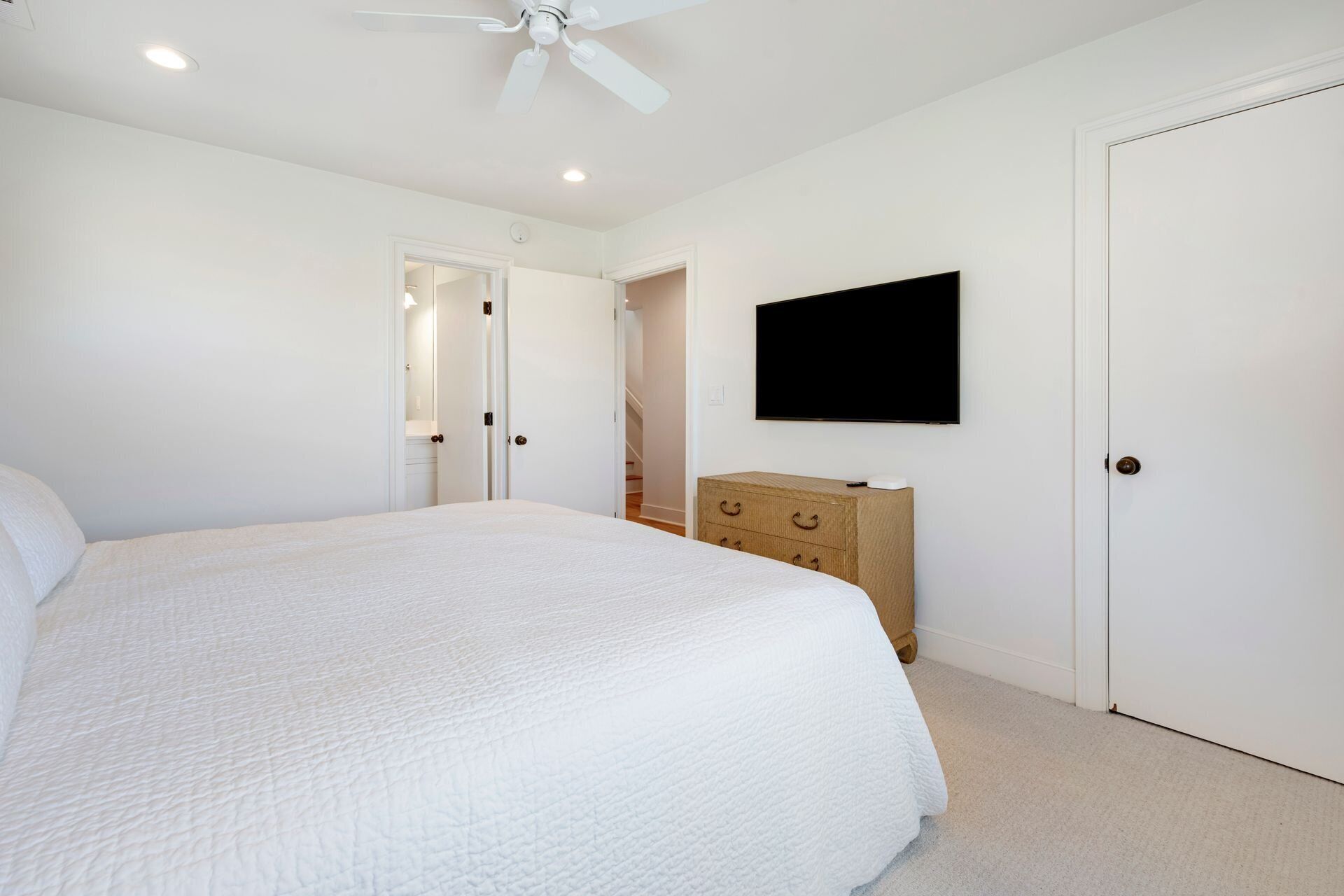 Ein Schlafzimmer mit einem großen Bett, einer Holzkommode, einem an der Wand montierten Fernseher und einem Deckenventilator.