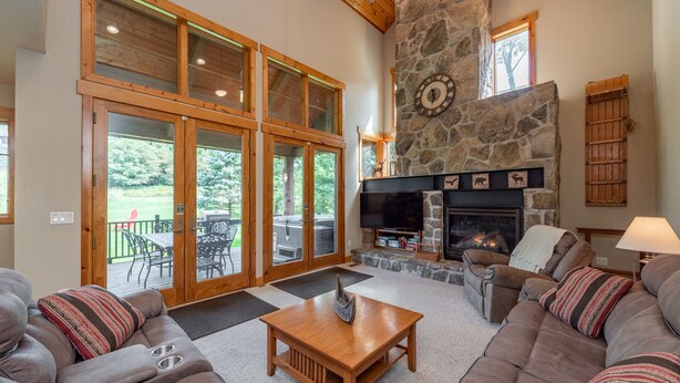 A spacious living room with a stone fireplace, large windows, and a cozy seating area.