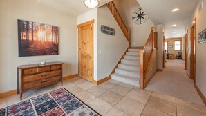 A hallway with a wooden staircase, a wooden dresser, a patterned rug, and a wall-mounted compass.