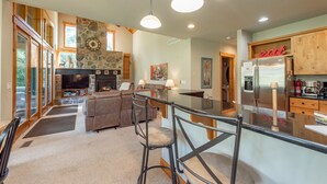 A spacious living area with a stone fireplace, a large TV, and a kitchen with wooden cabinets and a refrigerator.