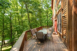 A wooden deck with a table and chairs, surrounded by a wooden railing, overlooking a forested area. - Spacious Deep Creek Stay w/ Rustic Charm (MCHENRY)