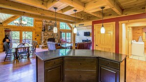 A spacious kitchen with a large island, wooden ceiling beams, and a stone fireplace. - Dog Friendly Home in Deep Creek Hills w/ Hot Tub (McHenry)