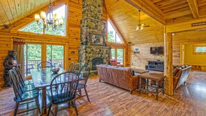 A log cabin interior with a stone fireplace, wooden dining table, and a cozy seating area. - Dog Friendly Home in Deep Creek Hills w/ Hot Tub (McHenry)