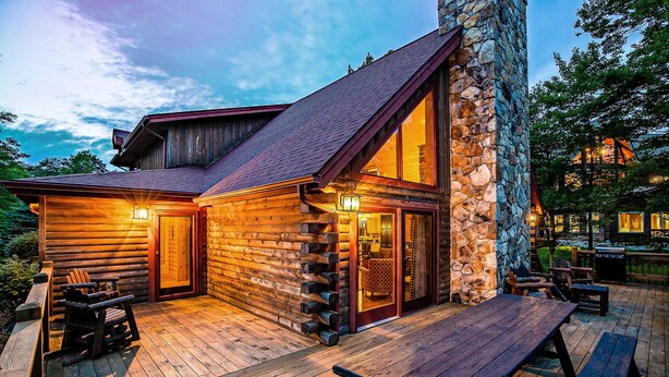 A log cabin with a stone chimney, wooden deck, and outdoor seating. - Dog Friendly Home in Deep Creek Hills w/ Hot Tub (McHenry)