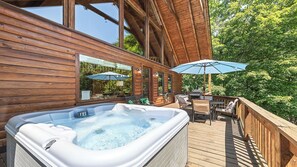 Eine Holzterrasse mit Whirlpool, Sitzgelegenheiten im Freien und Sonnenschirmen.