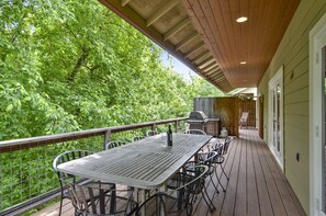 Een terras buiten met een houten dek, een tafel met stoelen, een barbecue en uitzicht op weelderige begroeiing.