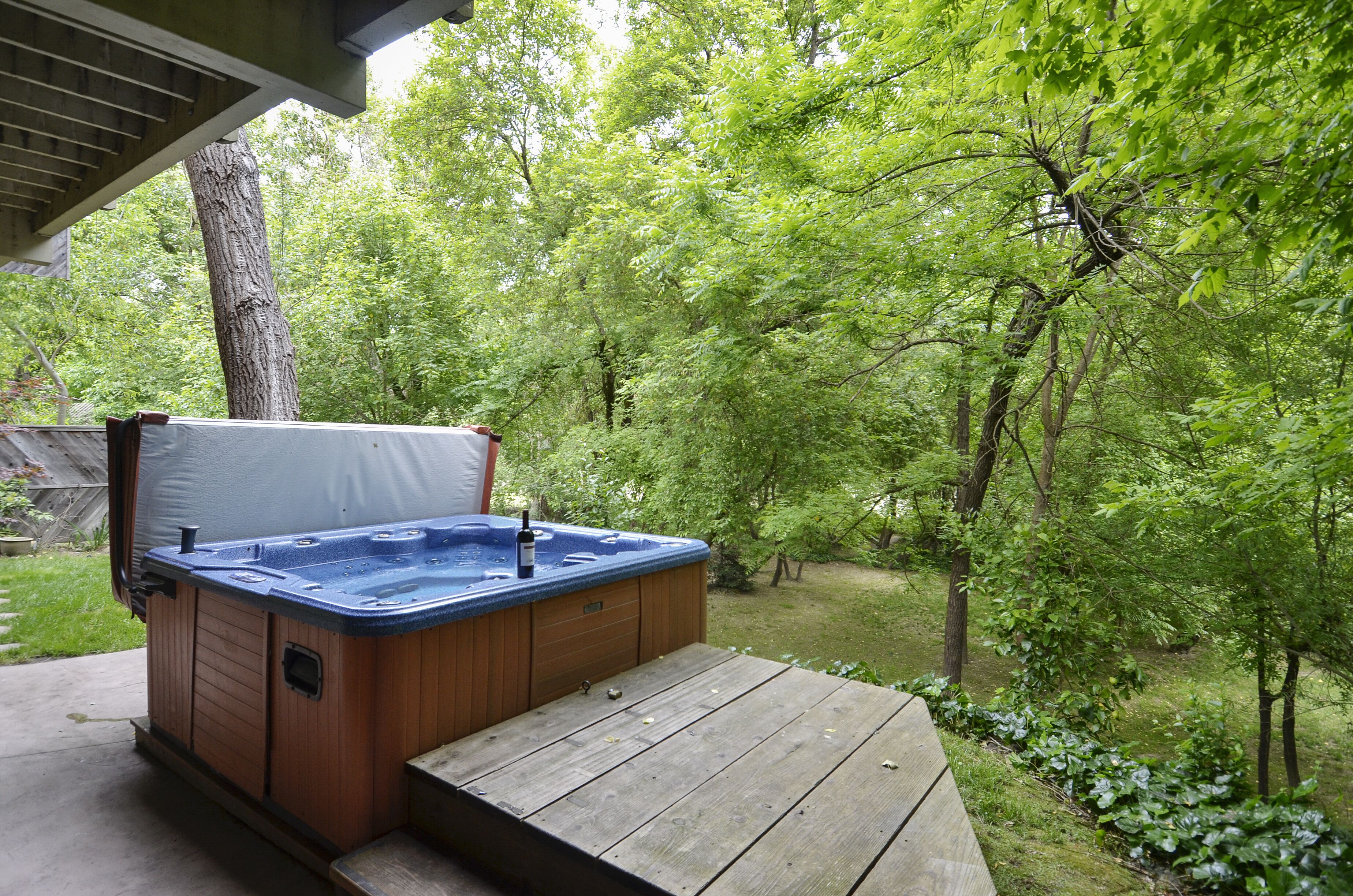A hot tub on a wooden deck surrounded by lush greenery.