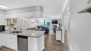 A modern kitchen with white cabinetry, a granite countertop, and a built-in dishwasher. - Ocean Dunes 2119 (Kure Beach)