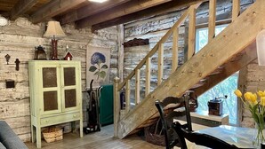 Un interior rústico de madera con una escalera, un armario verde y una mesa con flores amarillas.