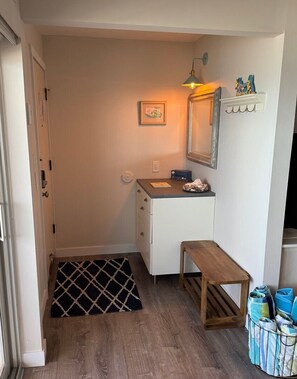 A compact room with a wooden bench, a small desk, a wall-mounted shelf with hooks, and a patterned rug.