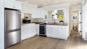 A modern kitchen with white cabinetry, stainless steel appliances, and a wooden floor. - Sand, Sun, Serenity P1111-23 (Oceanside)