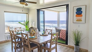 A dining area with a view of the ocean, wooden furniture, and a ceiling fan. - Sand, Sun, Serenity P1111-23 (Oceanside)
