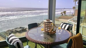 A glass table with a wicker chair, a glass candle holder, and two glasses with lemon slices. - Sand, Sun, Serenity P1111-23 (Oceanside)