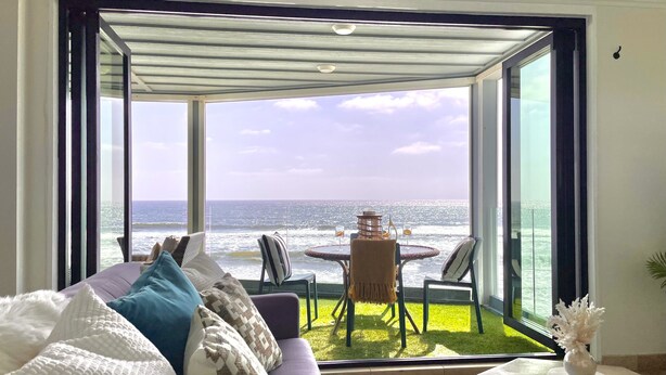 A living room with a large glass door leading to a balcony with a view of the ocean. - Sand, Sun, Serenity P1111-23 (Oceanside)