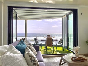 Relax in a spacious living room with a sofa, table, and chair, leading to an outdoor area with artificial grass and ocean views.