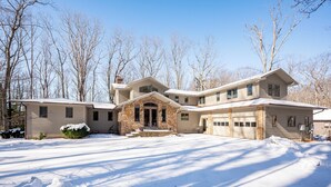 A large, two-story house with a stone entrance, multiple garage doors, and a snow-covered driveway. - Luxury Lake Escape in Quiet Cove w/ Dock (Oakland)