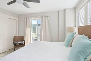 A hotel room with a bed, a chair, a ceiling fan, a window with curtains, and a view of the outdoors. - Oceanview Retreat, 302 (Tybee Island)