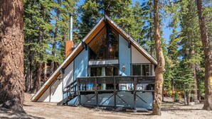 A cabin with a sloped roof, a balcony, and a chimney, surrounded by tall trees. - Chalet #25, Charming Ski in/ Ski Out, just steps to the Mountain (Mammoth Lakes)