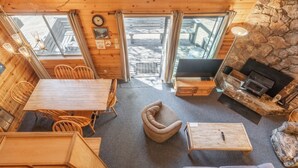 A cozy cabin interior with a dining area, a fireplace, and a stone wall. - Chalet #25, Charming Ski in/ Ski Out, just steps to the Mountain (Mammoth Lakes)