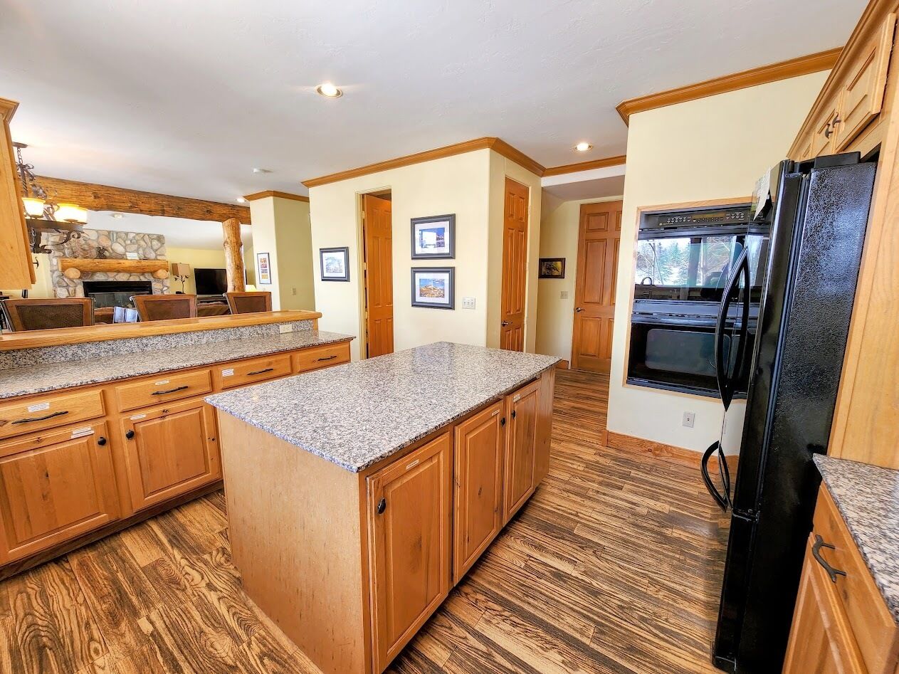 A spacious kitchen with wooden cabinets, granite countertops, and a black refrigerator.