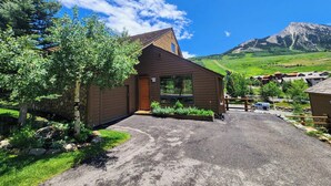 Une cabane en bois, construite sur des fondations en pierre, entourée d’un jardin bien entretenu et bordée d’une allée en gravier.