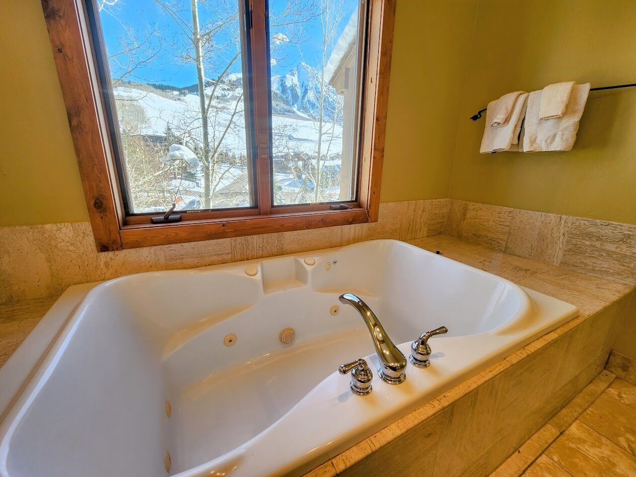 A bathroom with a large bathtub, a window with a view of snow-covered mountains, and a towel rack on the wall.
