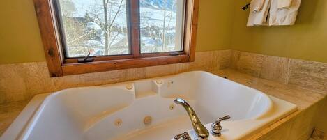 A bathroom with a large bathtub, a window with a view of snow-covered mountains, and a towel rack on the wall.