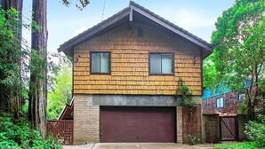 A two-story house with a brown shingle roof, a garage, and a fenced yard. - Eric's Landing ~ Riverfront, Fun with Friends Getaway! Dog Friendly! (Guerneville)