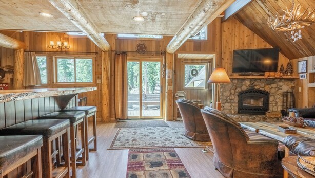 Interior rústico de una cabaña con barra, asientos, chimenea y televisor.