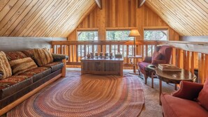 Una habitación acogedora estilo loft con techo y suelo de madera, un ventanal grande, un banco de madera, un sillón rojo y una alfombra tejida.
