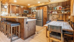 Una cocina rústica con armarios de madera, una isla central, taburetes de bar, un refrigerador y una mesa de comedor con sillas.