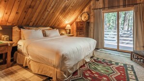 Un dormitorio acogedor con una cama grande, paredes de madera, una mesita de noche, una lámpara y vistas al exterior.