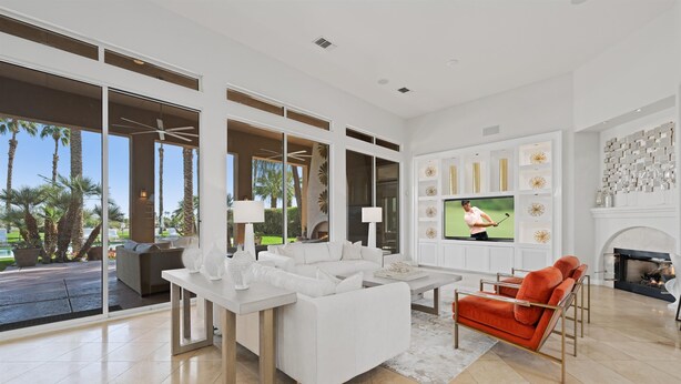 Una sala de estar moderna con un sofá blanco, un sillón rojo, una mesa de centro y un televisor que muestra un partido de golf.