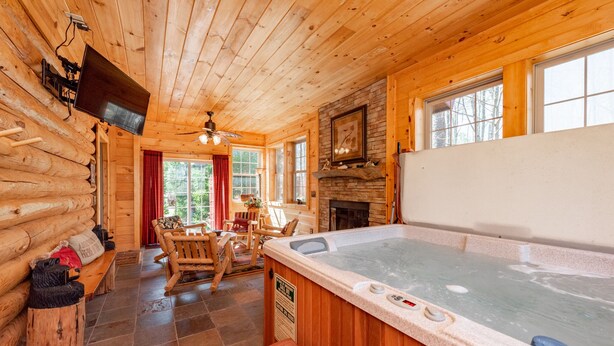 A log cabin interior with a hot tub, wooden furniture, a fireplace, and a television mounted on the wall.