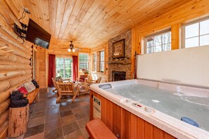 L’intérieur d’un chalet en bois comprend un bain à remous, des meubles en bois, une cheminée et un téléviseur fixé au mur.