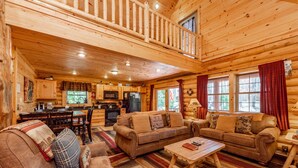 A log cabin interior with a dining area, kitchen, and two sofas with a coffee table.