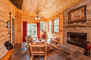 Un intérieur chaleureux de chalet en bois avec une cheminée en pierre, des meubles en bois et de grandes fenêtres.