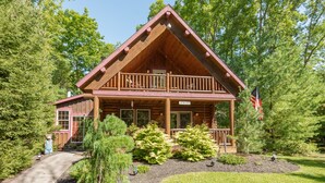 A log cabin with a balcony, surrounded by trees and a well-maintained garden.
