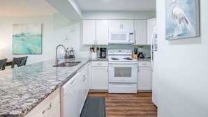 Una cocina moderna con armarios blancos, encimera de granito, microondas, horno y lavaplatos.