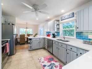 A modern kitchen with grey cabinets, a white countertop, a ceiling fan, and a 'Beach' sign.