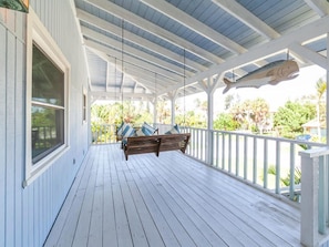 A covered porch with a swing chair and a hanging fish sculpture.