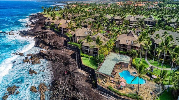 Un complejo turístico frente a la playa con villas, piscina y abundante vegetación.