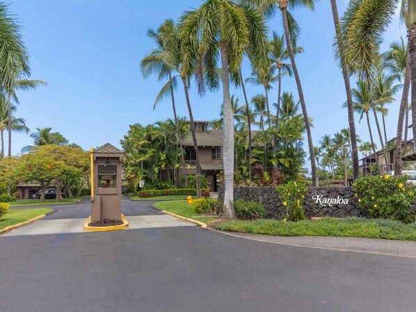 A gated entrance with a sign reading "Kailua," surrounded by palm trees and a well-maintained lawn.