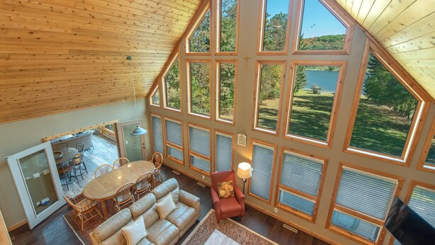 Quarto amplo com uma grande mesa de jantar, um sofá e uma poltrona vermelha. Há várias janelas grandes que oferecem vista para o exterior.